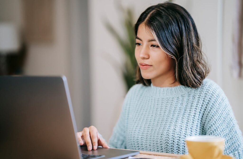 pexels-photo-6347902 Confident young Latin American woman in casual clothes working remotely on netbook at table near mug with coffee in light apartment with plant with green leaves near wall